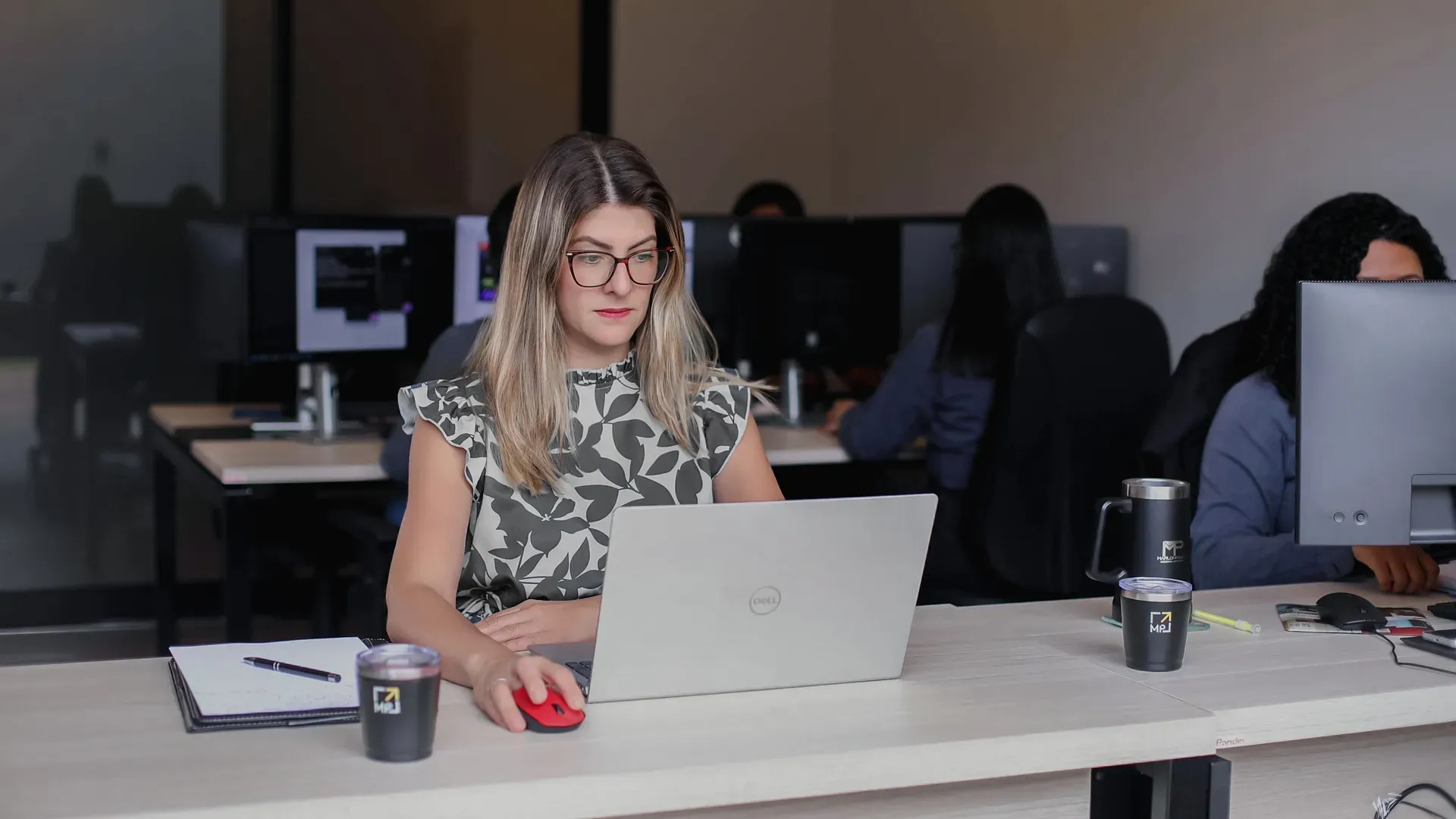 Profissional do escritório trabalhando no notebook, com a equipe ao fundo
